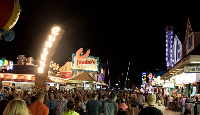 A crowd of people stroll through the Boardwalk at night.